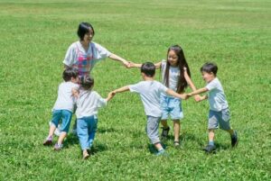 公園で輪になって遊ぶ保育士と子どもたち